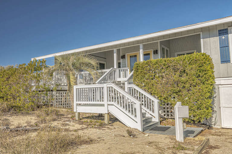 Sunlit Seaside Structure With Steps, Shrubs, And Sandy Setting