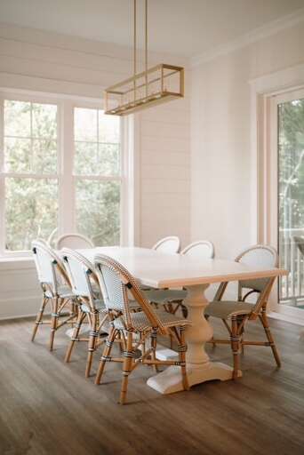 Bright Room With Big Windows And A White Round Table Surrounded By Wooden Chairs