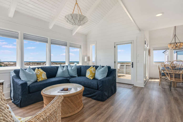Bright Beachside Living Room With Blue Sofa, Wooden Floors, And Large Windows Showing Sea Scenery