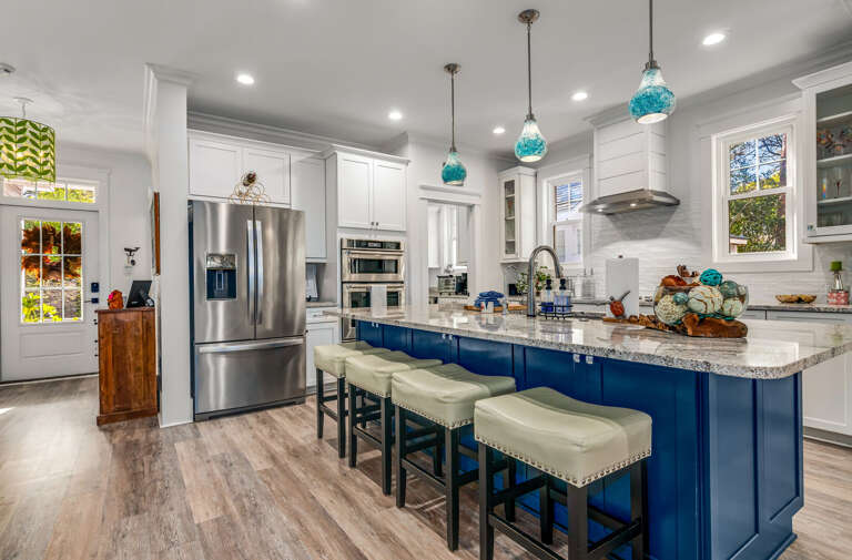 Spacious Kitchen With Blue Bar Stools And Bright Hanging Lights In A Vacation Rental