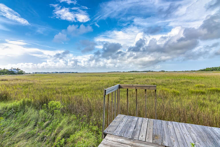 Wooden Walkway Winds Through Vast Vivid Marsh Under Expansive Cloud-covered Sky