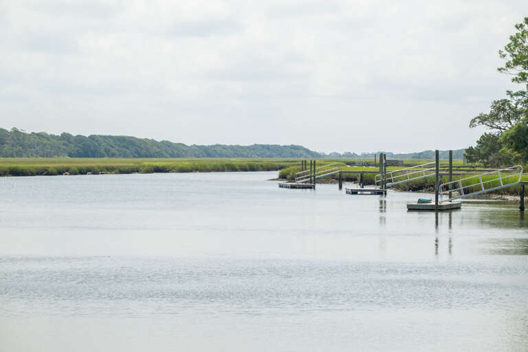 Serene Scene Of Still Waters With Slender Docks And Lush Landscape