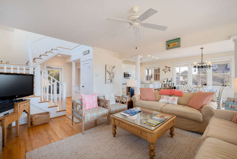 Bright Beachside Living Area With White Walls And Light Furniture, Featuring A Staircase And Ceiling Fan