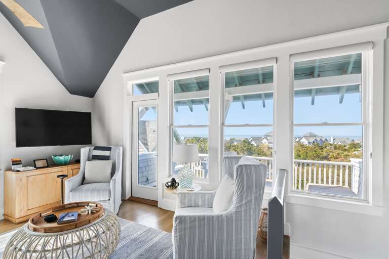 Bright Room With Large Windows, Striped Chairs, Round Table, And Wall-mounted TV