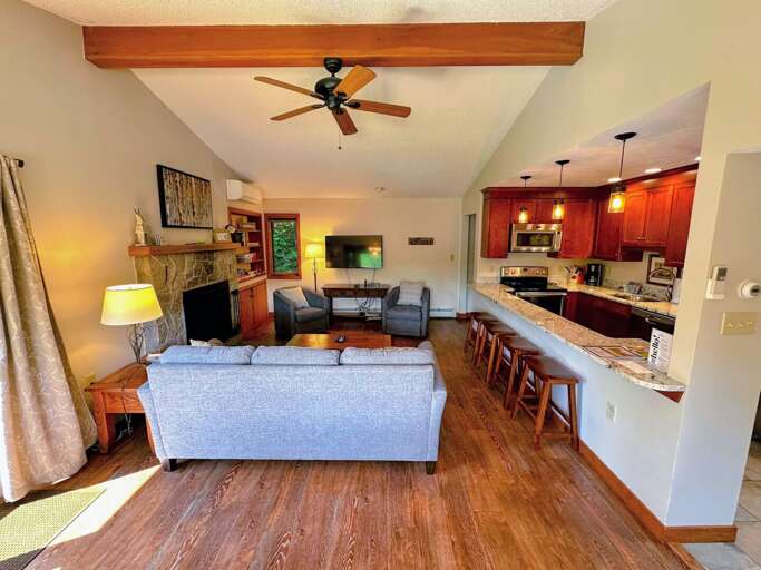 The living room is outfitted with a wood burning fireplace, TV and AC adjacent to a convenient breakfast bar and dining table
