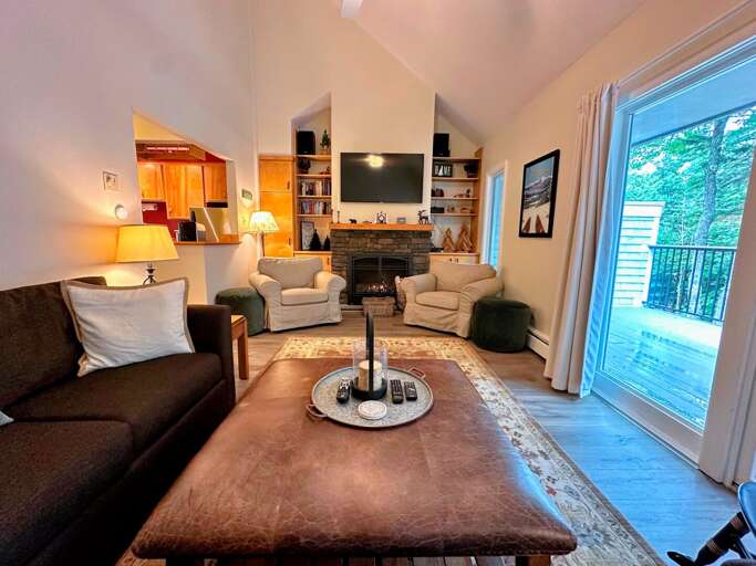 Main level living room with TV, gas fireplace, and walkout to deck