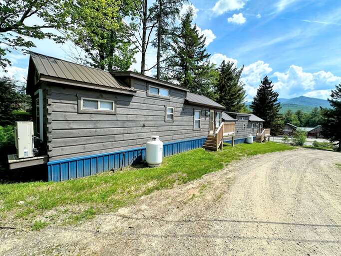 Rural Lodging Buildings Beside Dirt Road With Trees And Mountain In Background