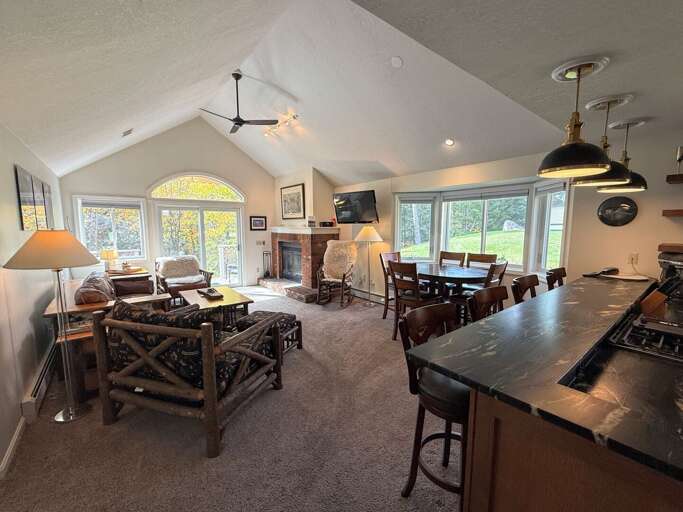 Gather in the airy living and dining area, with vaulted ceilings, large windows, and breakfast-bar seating beside the kitchen.