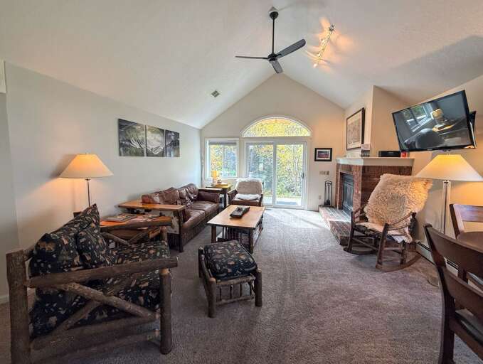 Relax in the bright living room with rustic seating, a brick fireplace, wall-mounted TV, and sliding doors to the deck.