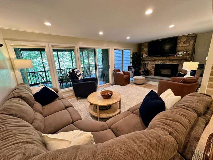 Main level living area with comfortable seating, TV, wood burning fireplace, and walkout deck