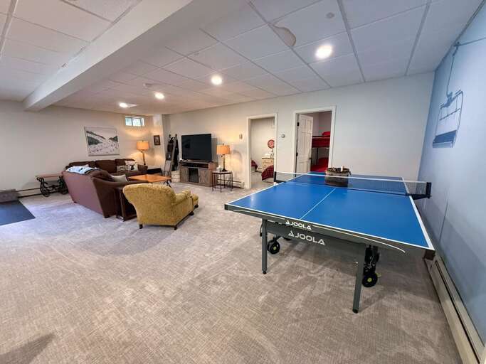 A second gathering space downstairs offers comfortable seating, a TV, a ping pong table, and walkout access to the parking area.