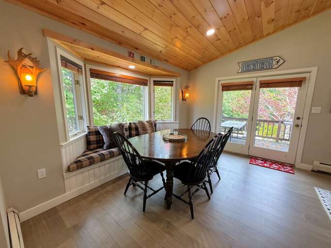 Share meals around the dining table, with seating for 6-8, a cushioned window bench, and deck access nearby.