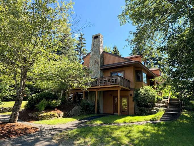 A summer view of the cottage, showing the deck, lower-level entrance, and steps to the main level.