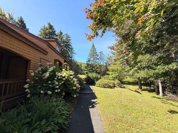 A view from the main entrance toward the ski trail shows the cottage's lawn, walkway, and wooded setting.