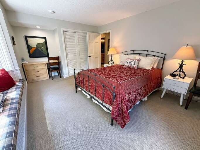 Another view of the main-level queen bedroom, with a small desk, dresser, and closet storage.