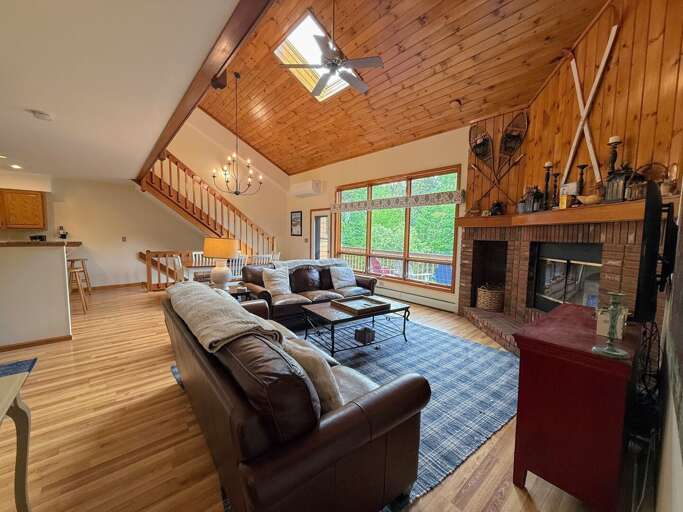 Main Level Living room offers comfortable seating, a wood burning fireplace, and TV. It's in an open-concept main area adjacent to the dining room and kitchen.
