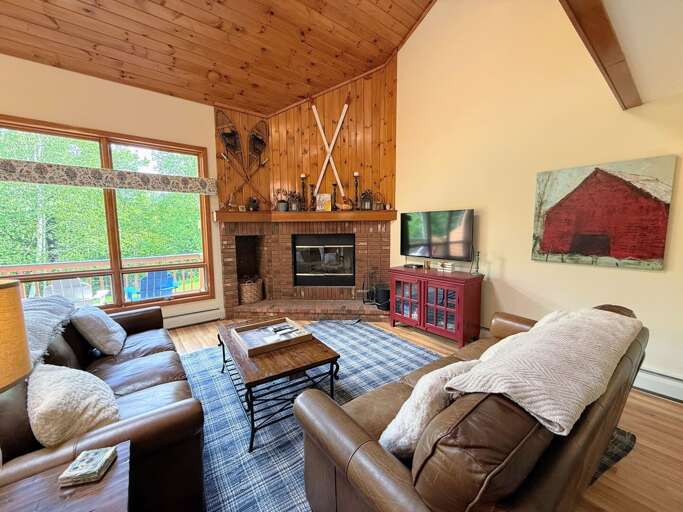 Main Level Living room offers comfortable seating, a wood burning fireplace, and TV. It's in an open-concept main area adjacent to the dining room and kitchen.