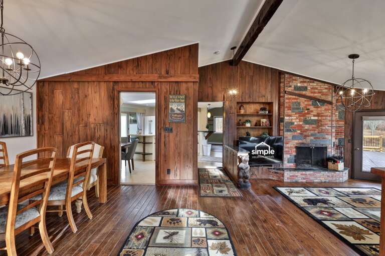 Warm, rustic interior with wood paneling, brick fireplace, exposed beam overhead, iron light fixtures and wood floors. The kind of lived-in comfort people crave after a cold mountain day.