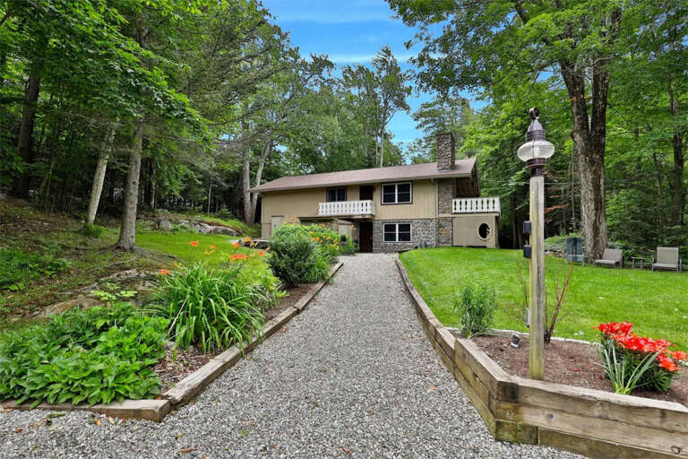 Summer exterior view of our ski home in Killington, Vermont. A large vacation home surrounded by trees, bushes and lawn, with large windows and outdoors decks.
