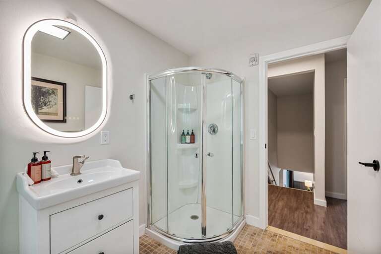 The compact vanity sits beside the curved shower, with the bedroom just beyond the door.