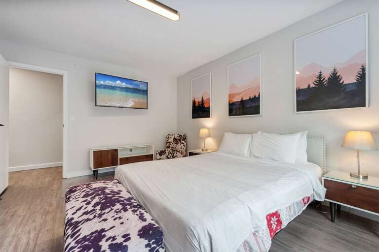 A low console and wall-mounted TV sit directly across from the bed.