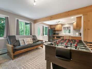 Entertainment area with sofa, foosball table, Smart TV and sunlight from many windows.