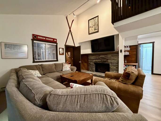 Open living room with vaulted ceilings, a gas fireplace, and a large wall-mounted smart TV for family movies.