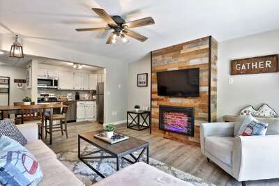 Renovated living room, with a smart TV and electric fireplace, of this modern 3-bedroom condo at Mountain Green Resort, Killington, VT, with the open kitchen and dining area seen in the back.