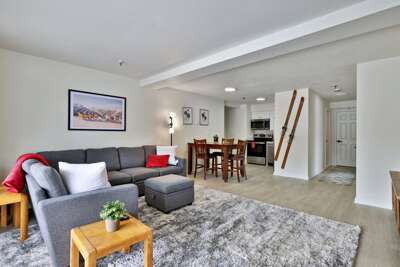 Spacious living room with plenty of seating, an open kitchen and dining area, plus a large plush gray-toned rug.