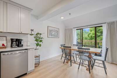 The dining area sits between the kitchen and balcony doors, with treetop views just outside.