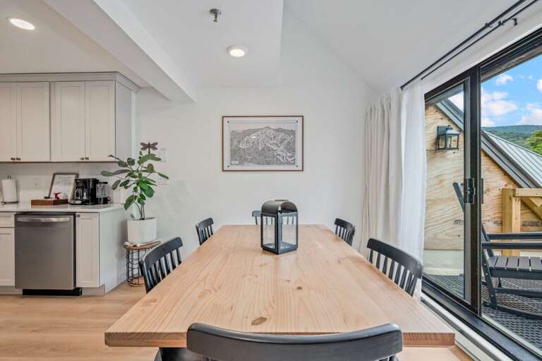 The long dining table anchors the open room, with the kitchen and balcony on either side.