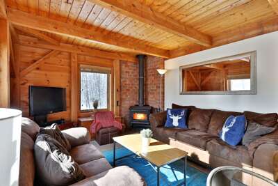 Living room of our wood-beam home nestled in the Green Mountains of Vermont, with plentiful comfy seating in front of the smart TV and stove.