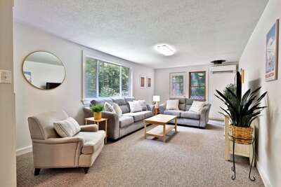 Living room in soft gray tones, with several sofas, stylish modern décor, large windows and a Smart TV.