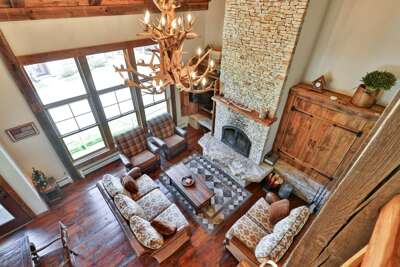 Stylish living room with a wood-burning fireplace, chimney clad with mountain stack stone veneer, an Antler Chandelier, cozy seating, and relaxing mountain views.