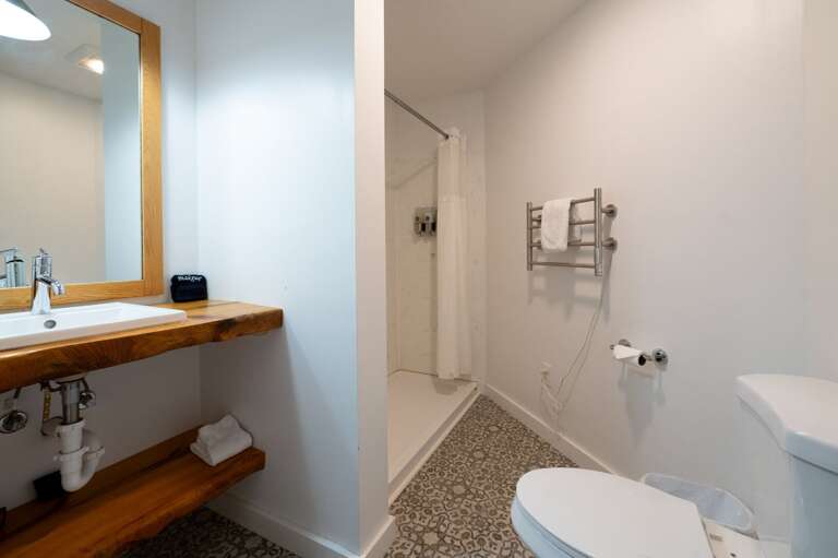 Bathroom with an open wood vanity, walk-in shower, toilet, and patterned tile floor.