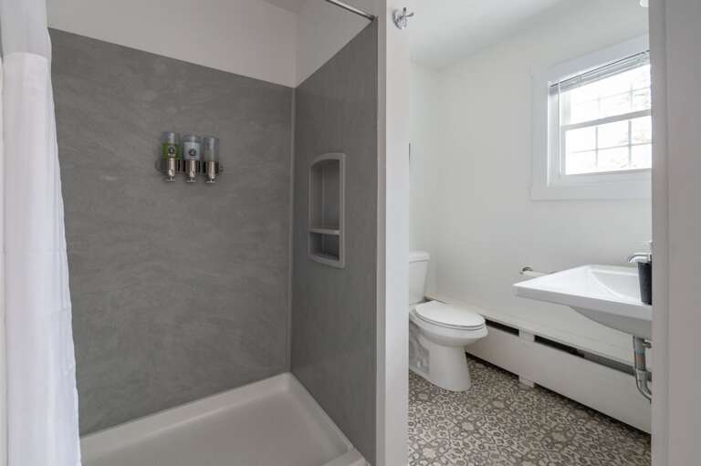 Bathroom with a walk-in shower, toilet, open vanity, window, and patterned tile floor.
