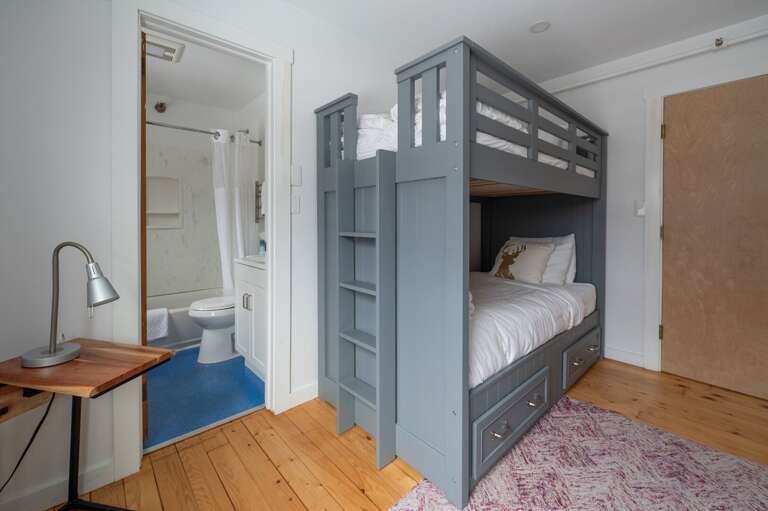 Bunk room with a sturdy bunk bed, small desk, and doorway to a bathroom.