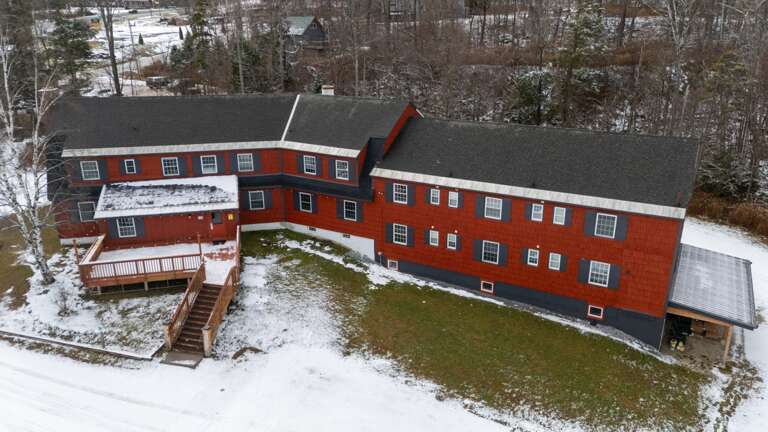 The front aerial perspective shows the lodge, decks, and broad snowy arrival area together.