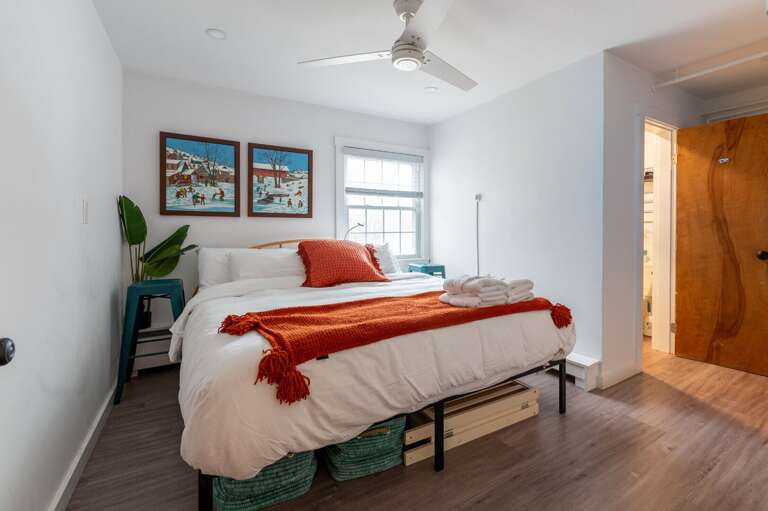 Guest bedroom with a bed, ceiling fan, dresser, and doorway to an en suite bathroom.