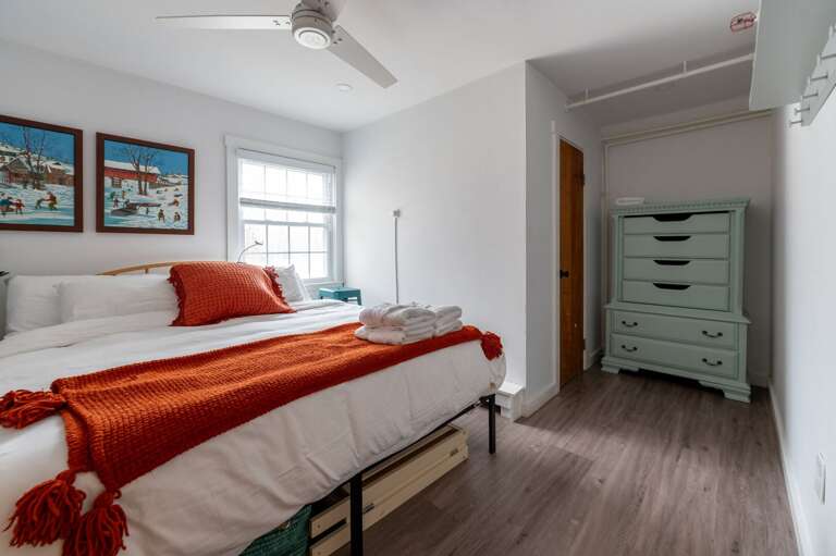 Guest bedroom with a bed, ceiling fan, side table, and tall chest of drawers.