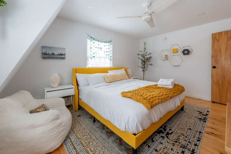 Guest bedroom with a bed, side tables, floor seating, ceiling fan, and window.