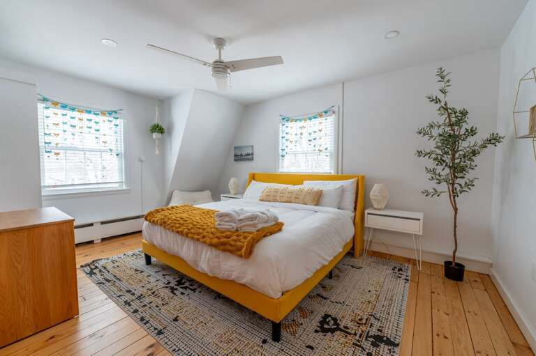 Guest bedroom with a bed between two windows, ceiling fan, side tables, and hardwood floor.