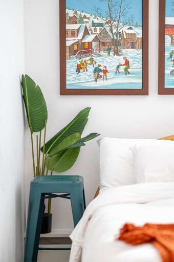 Guest bedroom corner with a bed, side table, framed ski artwork, and decorative plant.