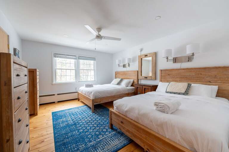 Guest bedroom with two wood-frame beds, dresser, vanity, ceiling fan, and area rug.
