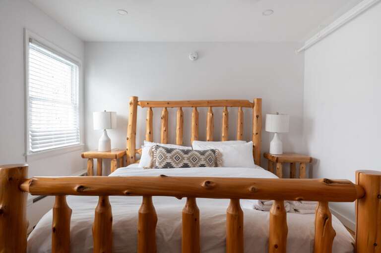 Log-frame bed with bedside lamps, a window, and hardwood floor.