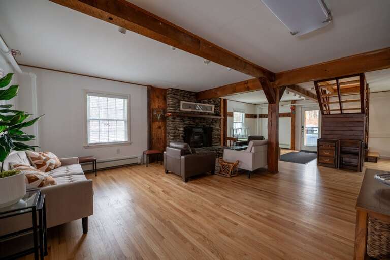 Main living room with a stone fireplace, multiple seating areas, exposed beams, and a central staircase.
