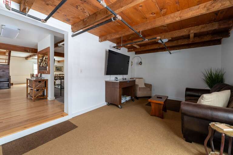 Secondary TV lounge with a wall-mounted television, seating, and an exposed wood ceiling.