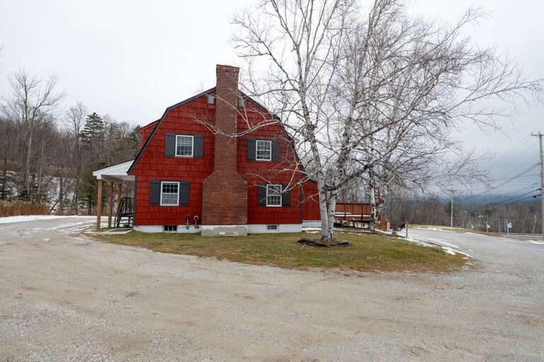 Side exterior of The Birch Tree Lodge with red siding, large windows, a birch tree, and driveway.