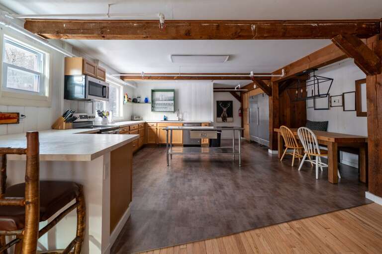 Wide kitchen view with counter seating, a central prep island, dining space, and exposed timber beams.