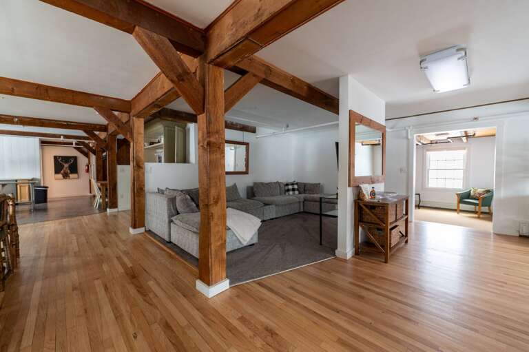 Wide living room view with timber columns, sectional seating, a TV, and an adjacent sitting area.